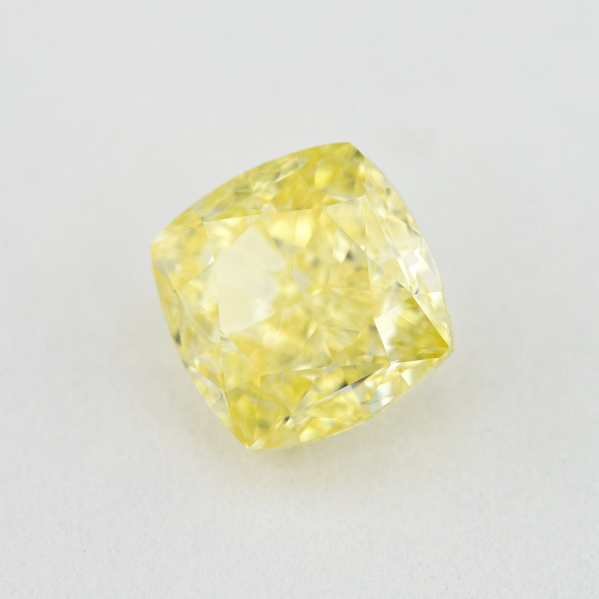 Angled crown view of the cushion-shaped yellow diamond on a pale surface, with bright reflected facets.