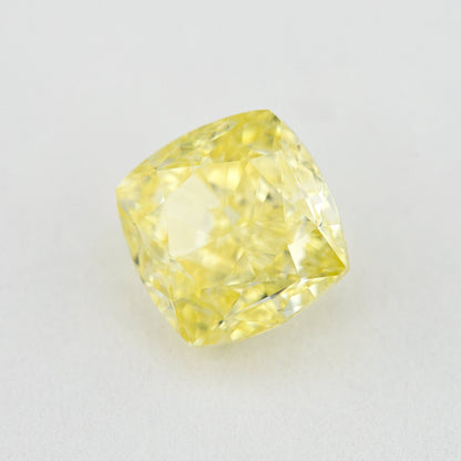 Angled crown view of the cushion-shaped yellow diamond on a pale surface, with bright reflected facets.