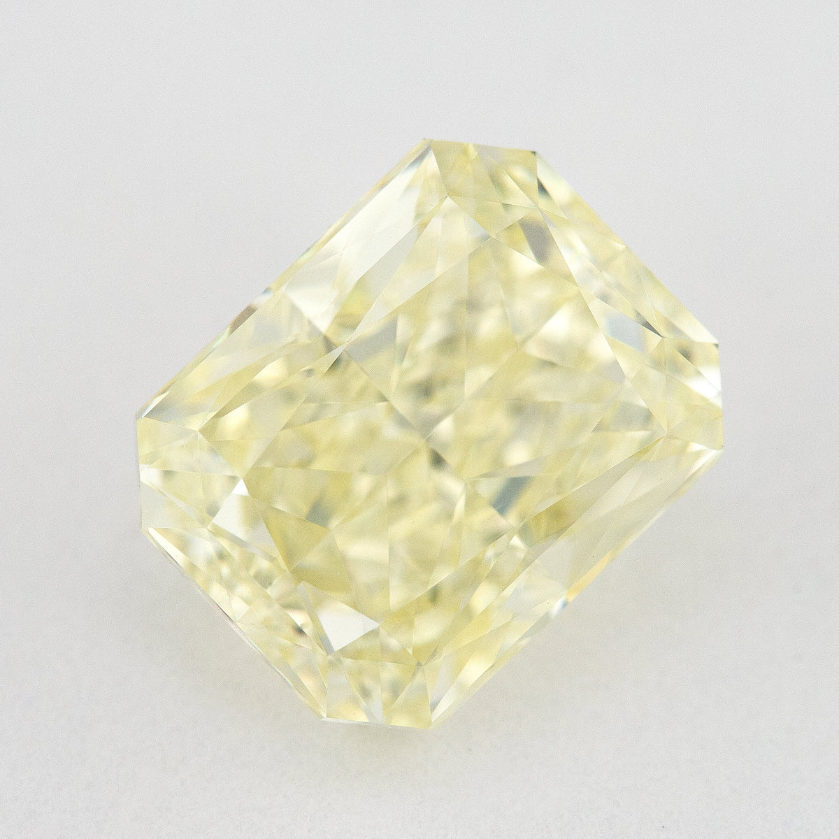 Face-up view of a pale yellow rectangular radiant-cut natural diamond on a pale surface, showing its complete outline and crown facets.
