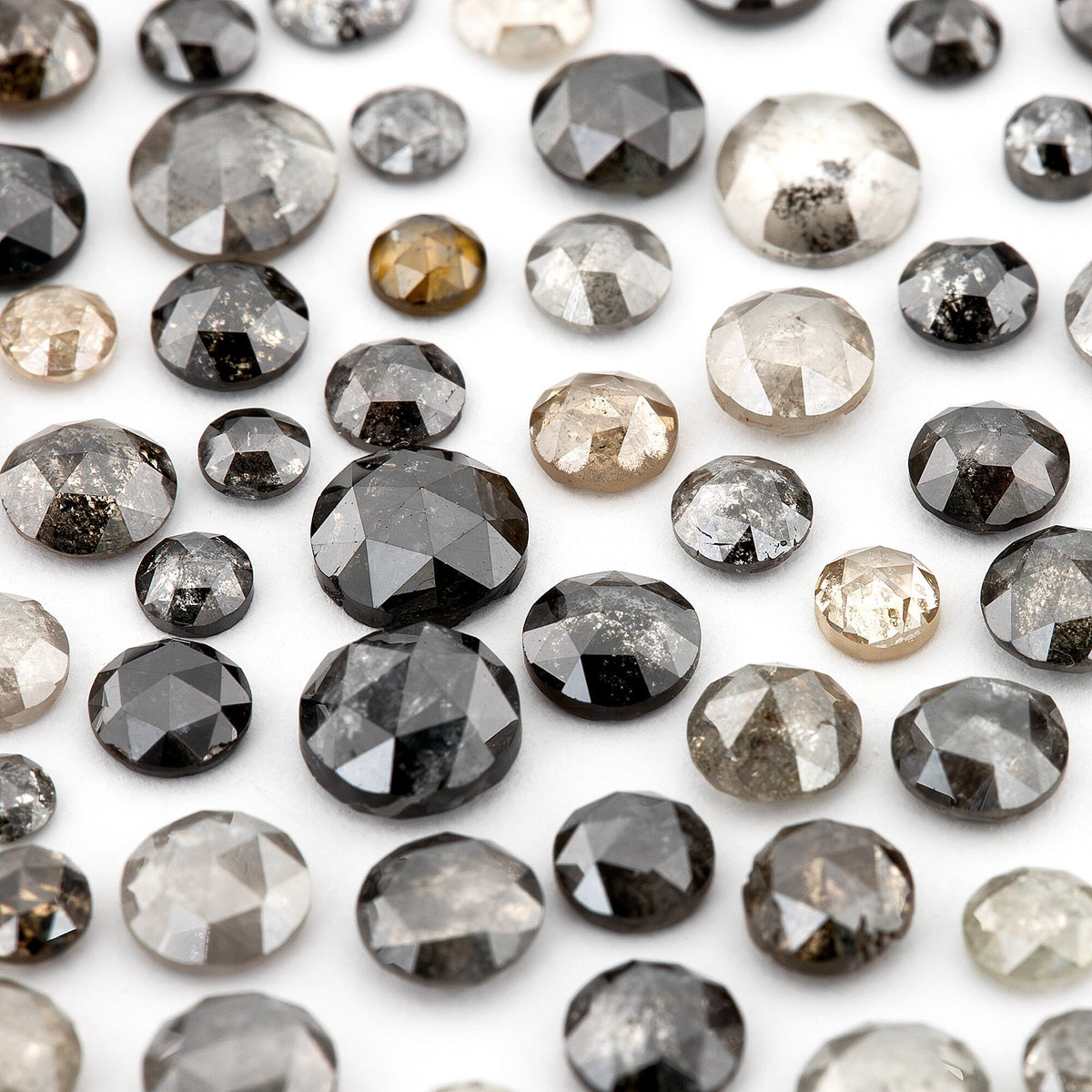Close view of mixed grey and black rose-cut diamonds with visible internal markings; individual one-carat scoop contents vary.