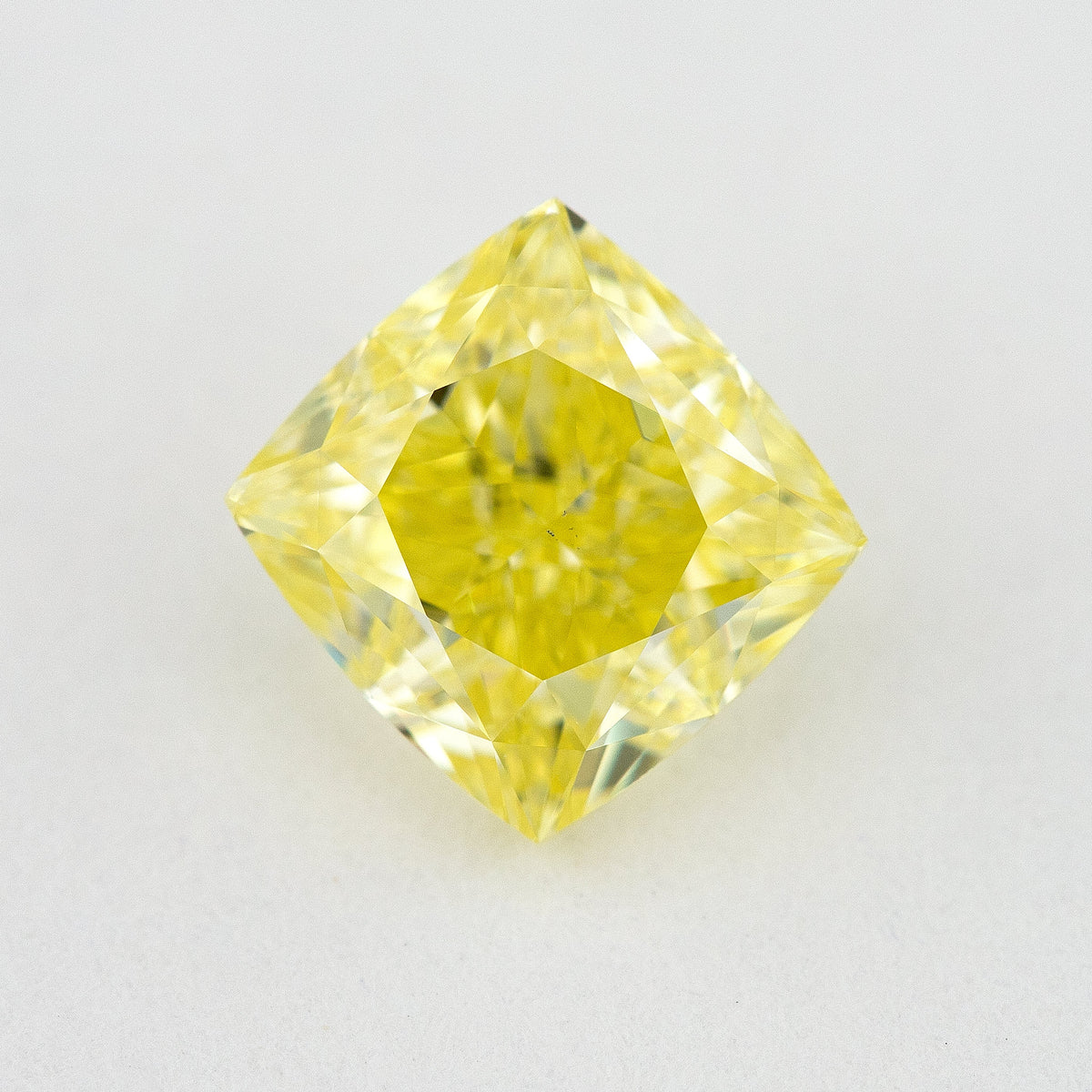 Face-up cushion-shaped yellow diamond on a pale surface, showing its complete outline, table and crown facets.