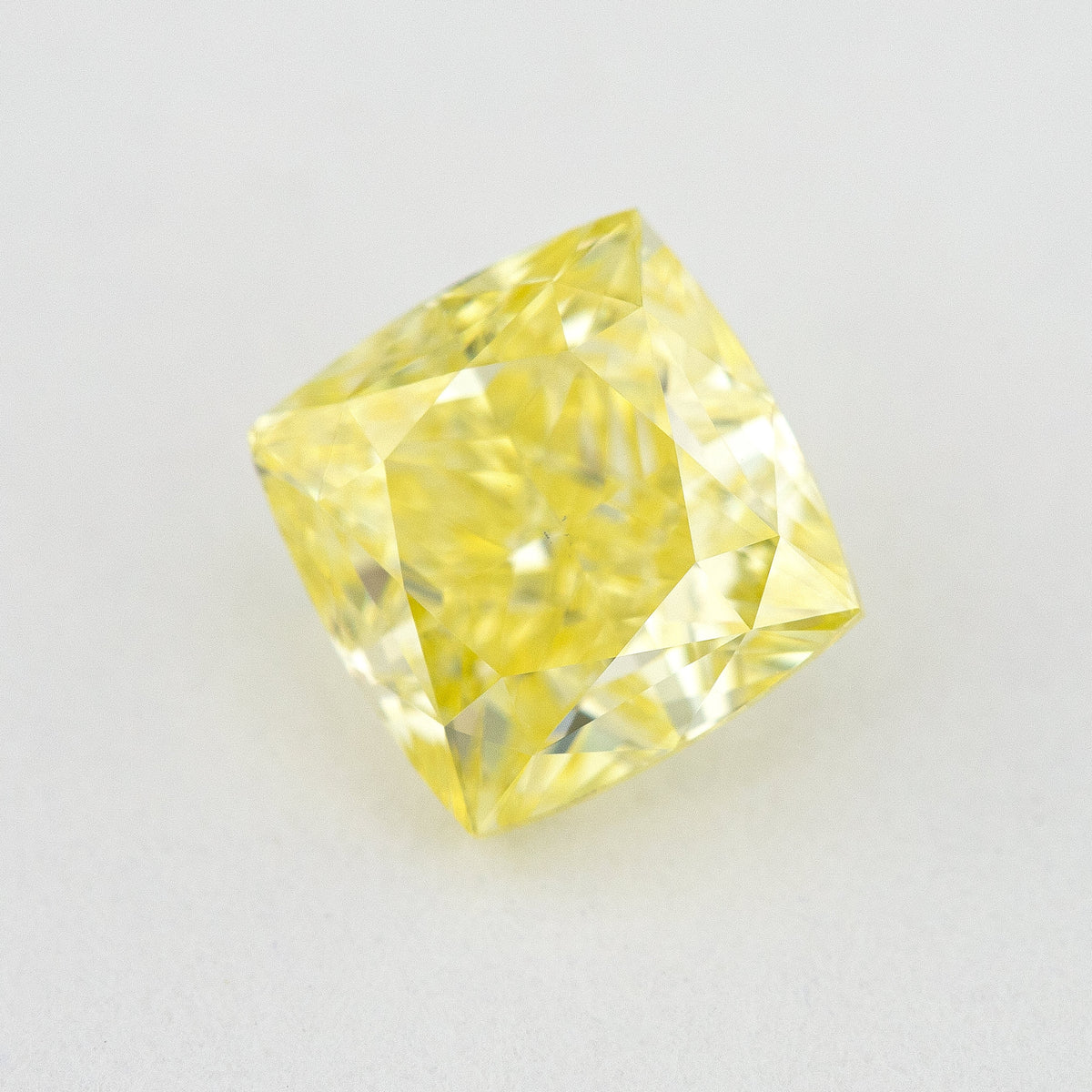 Angled crown view of the cushion-shaped yellow diamond on a pale surface, with bright reflected facets.