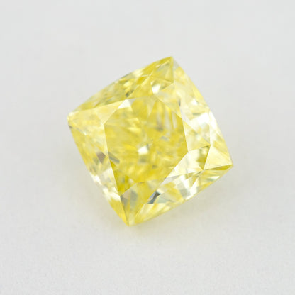Angled crown view of the cushion-shaped yellow diamond on a pale surface, with bright reflected facets.