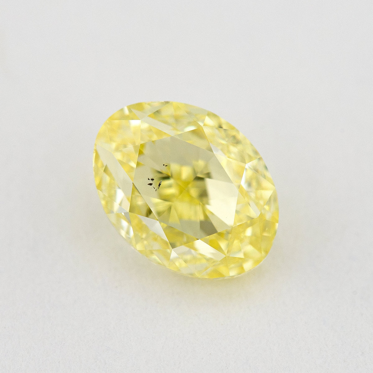Face-up oval yellow diamond on a pale background, with a visible dark inclusion cluster near the center.