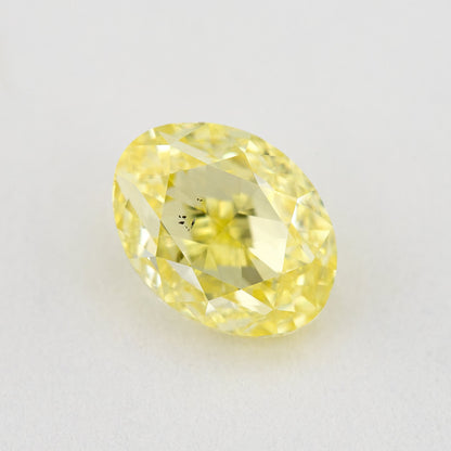 Face-up oval yellow diamond on a pale background, with a visible dark inclusion cluster near the center.