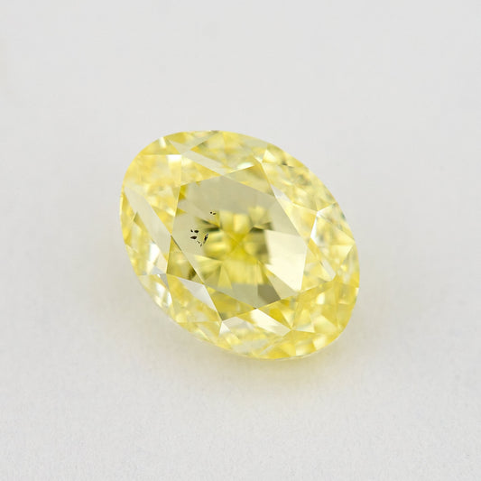 Face-up oval yellow diamond on a pale background, with a visible dark inclusion cluster near the center.