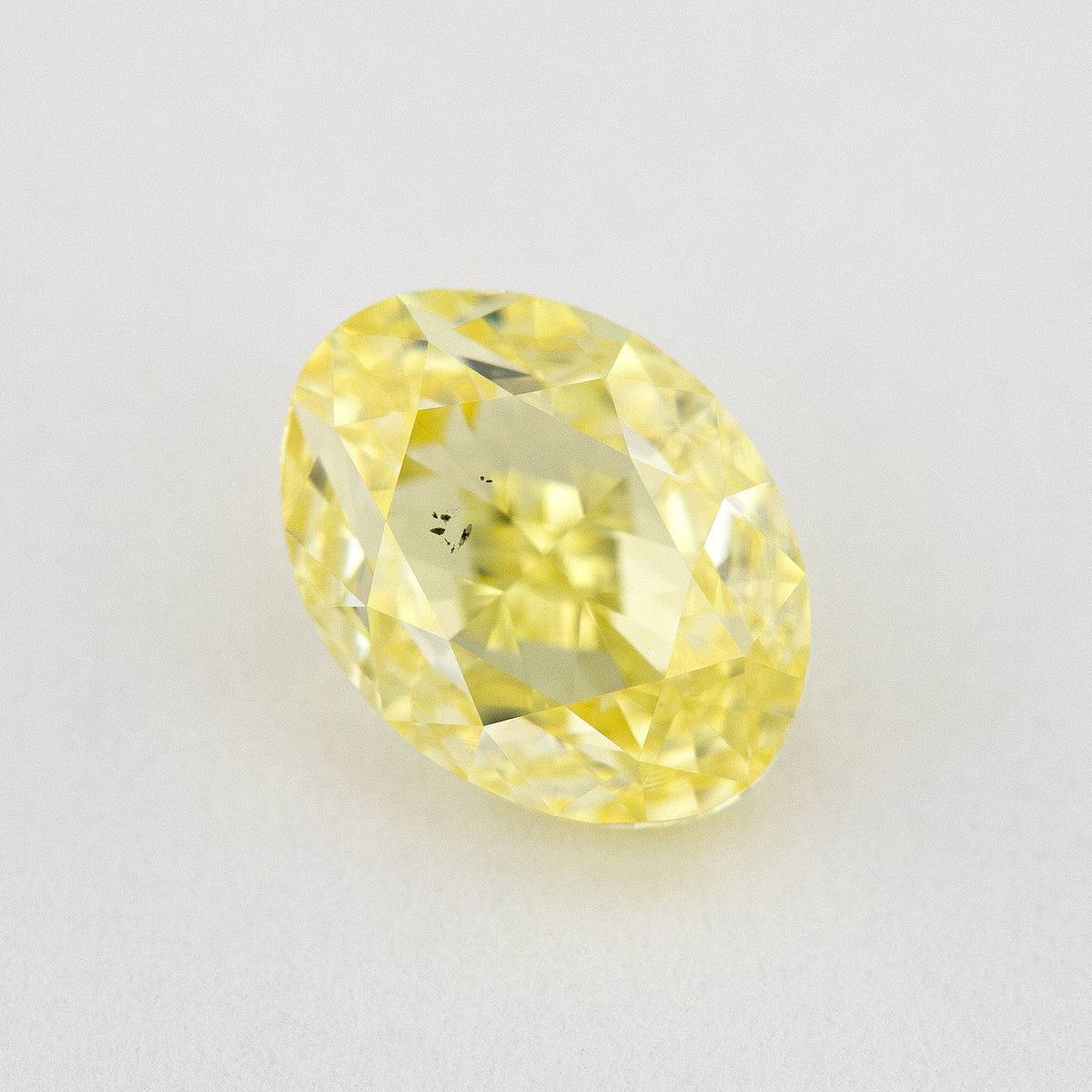 Oval yellow diamond rotated on a pale background, showing a different face-up reflection and visible inclusions.