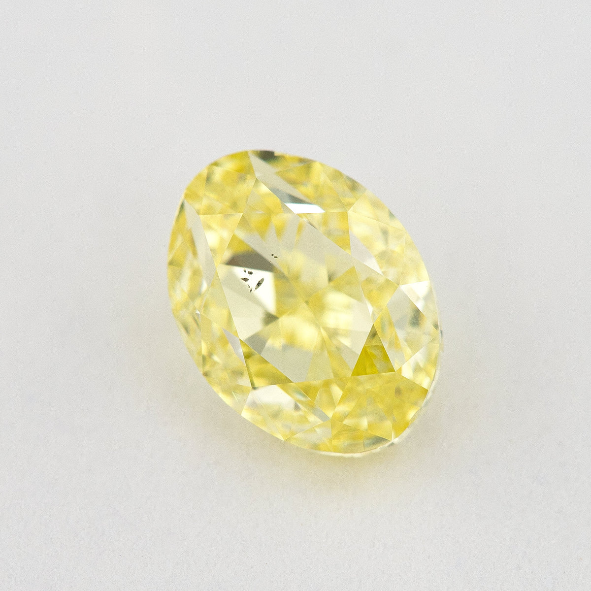 Upright face-up view of the oval yellow diamond, with brilliant facets and a dark inclusion cluster.