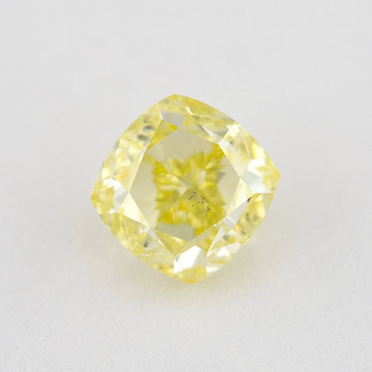 Face-up near-square cushion-shaped yellow diamond on a pale background, with visible dark inclusions.