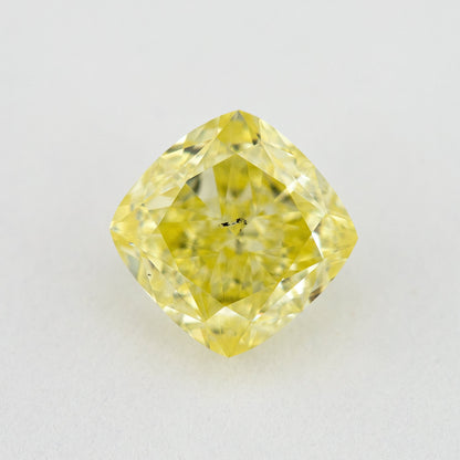 Face-up cushion-shaped yellow diamond on a pale surface, with small dark marks visible near the centre.