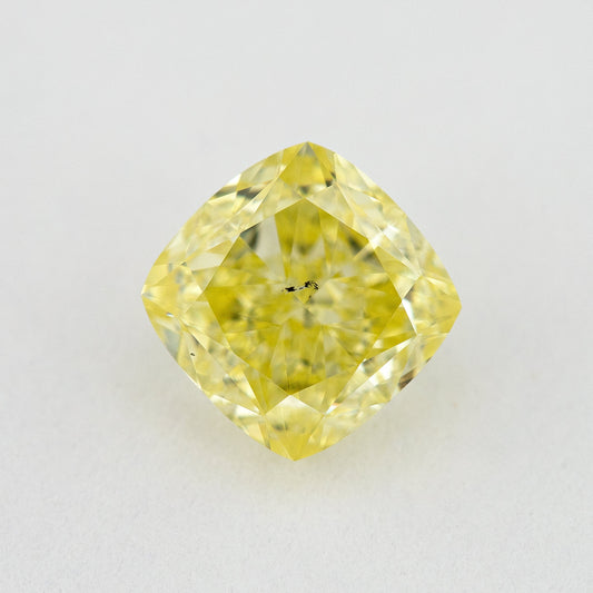 Face-up cushion-shaped yellow diamond on a pale surface, with small dark marks visible near the centre.