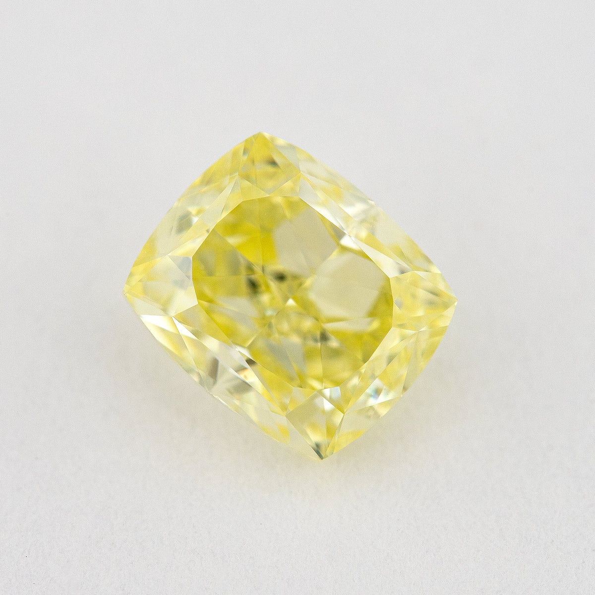 Face-up close-up of the yellow cushion diamond on a pale background, showing its complete outline and crown facet reflections.