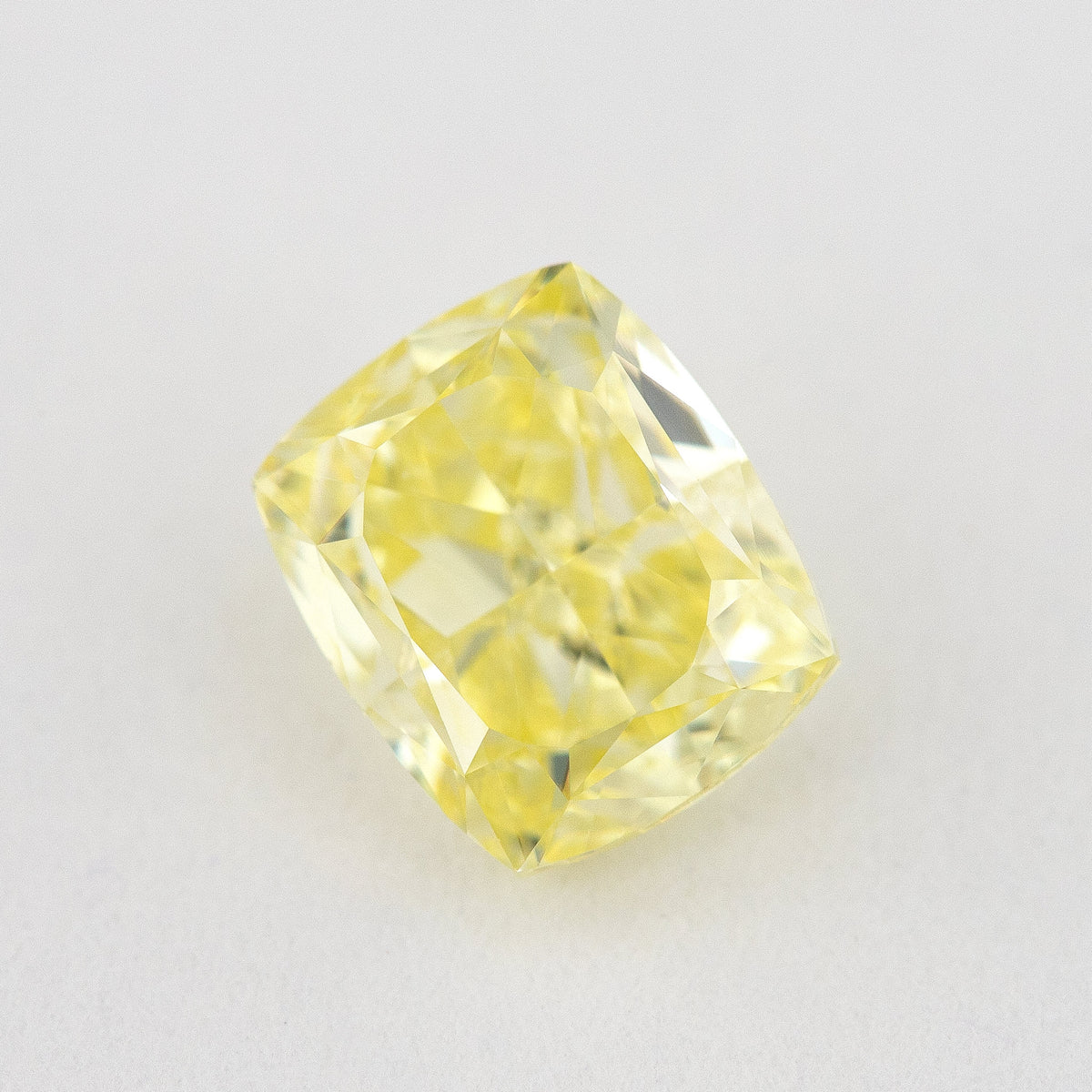 Alternate angled face-up view of the yellow cushion diamond on a pale background, with a different pattern of light and dark facet reflections.