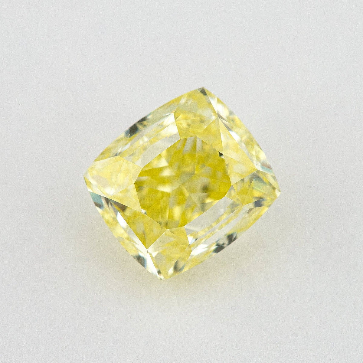 Face-up cushion-shaped yellow diamond on a pale background, showing the complete outline and broad table.