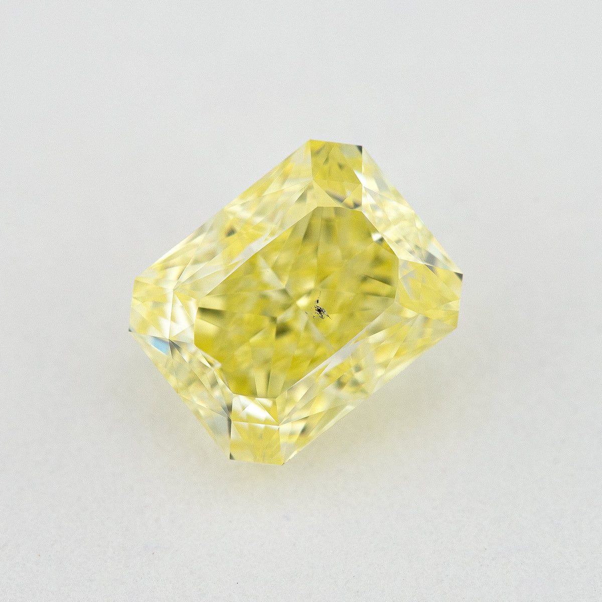Face-up radiant-cut yellow diamond on a pale surface, showing its cut-cornered rectangular outline and crown facets.