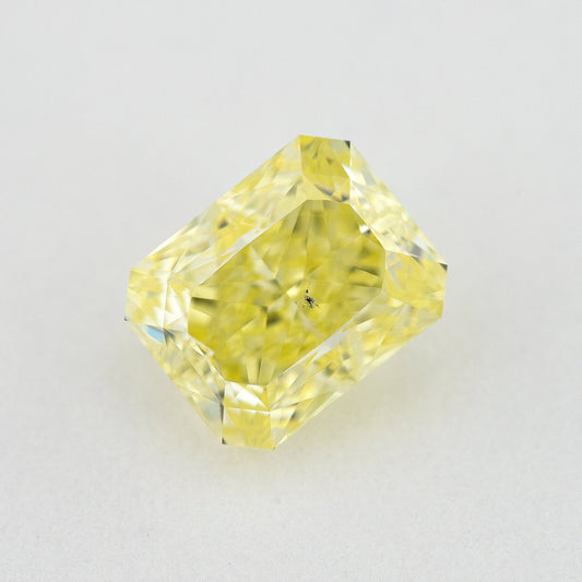 Face-up radiant-cut yellow diamond on a pale surface, showing its cut-cornered rectangular outline and crown facets.