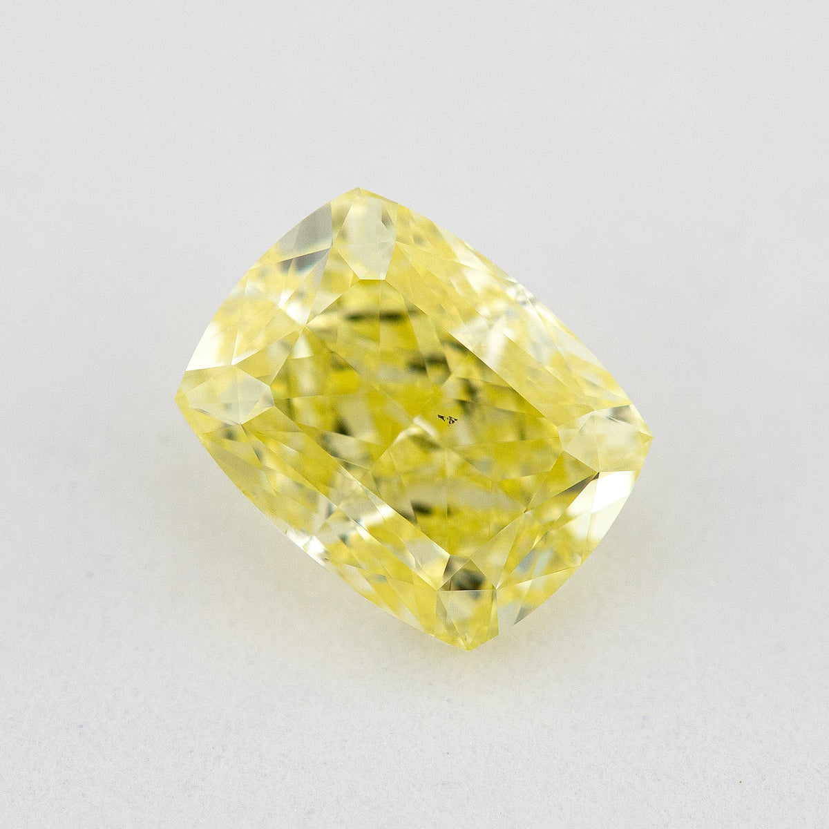 Face-up elongated cushion-shaped yellow diamond on a pale surface, with small dark marks visible near the centre.