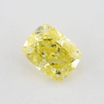 Face-up elongated cushion-shaped yellow diamond on a pale surface, with small dark marks visible near the centre.
