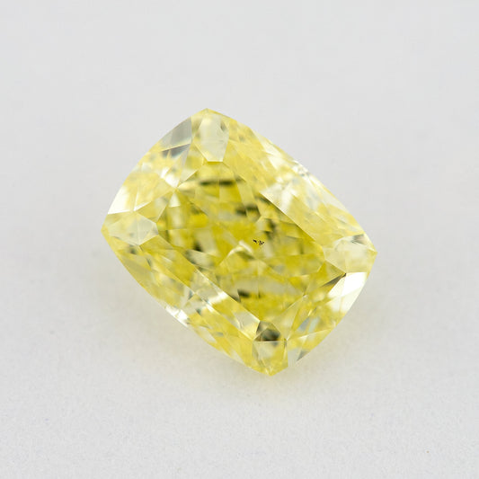 Face-up elongated cushion-shaped yellow diamond on a pale surface, with small dark marks visible near the centre.