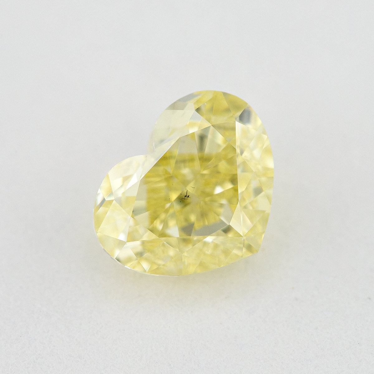 Face-up heart-shaped yellow diamond on a pale surface, showing its cleft, pointed end and small dark central marks.