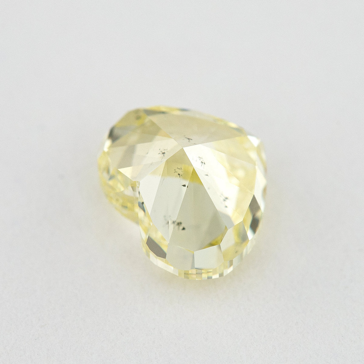 Pavilion and back view of the heart-shaped yellow diamond, showing broad rear facets and small dark marks.
