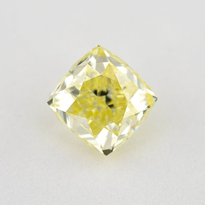 Face-up cushion-shaped yellow diamond on a pale surface, showing bright crown facets and dark central reflections.
