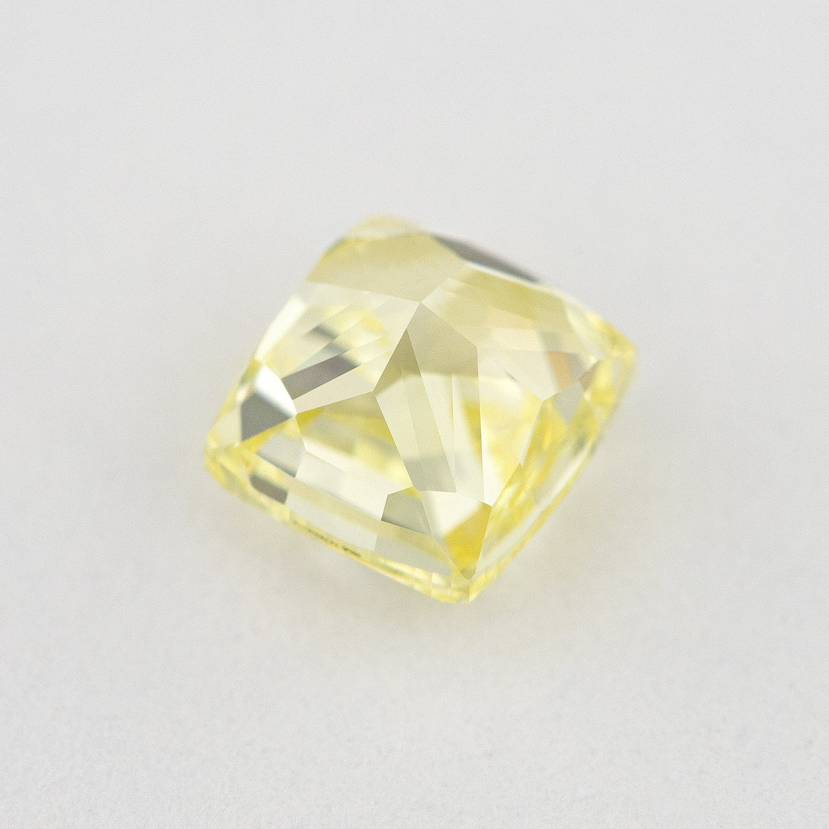 Pavilion and back view of the cushion-shaped yellow diamond, showing broad rear facets on a pale surface.