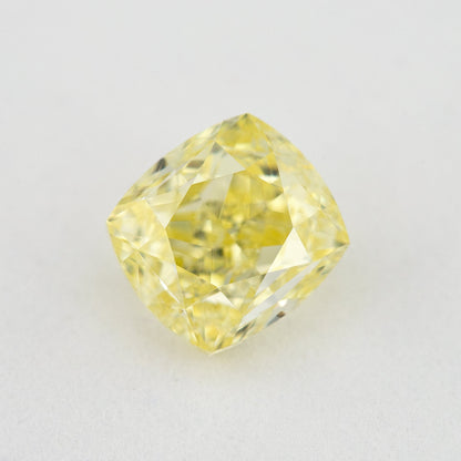 Face-up cushion-shaped yellow diamond on a pale surface, showing its complete outline, table and crown facets.