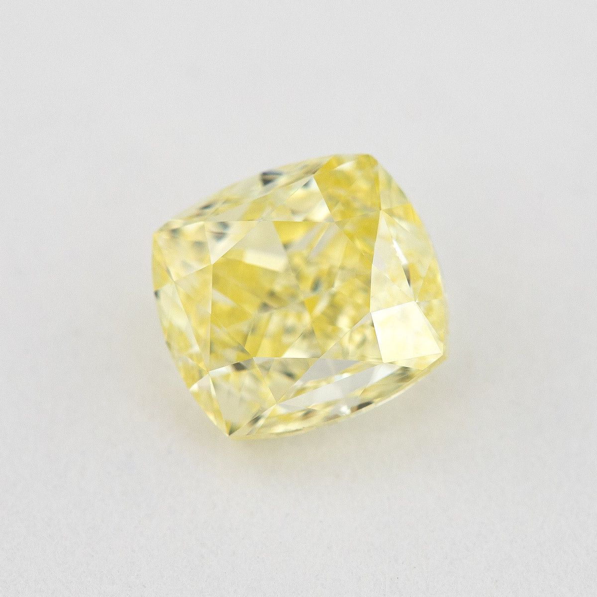 Angled crown view of the cushion-shaped yellow diamond on a pale surface, with bright reflected facets.