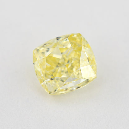 Angled crown view of the cushion-shaped yellow diamond on a pale surface, with bright reflected facets.