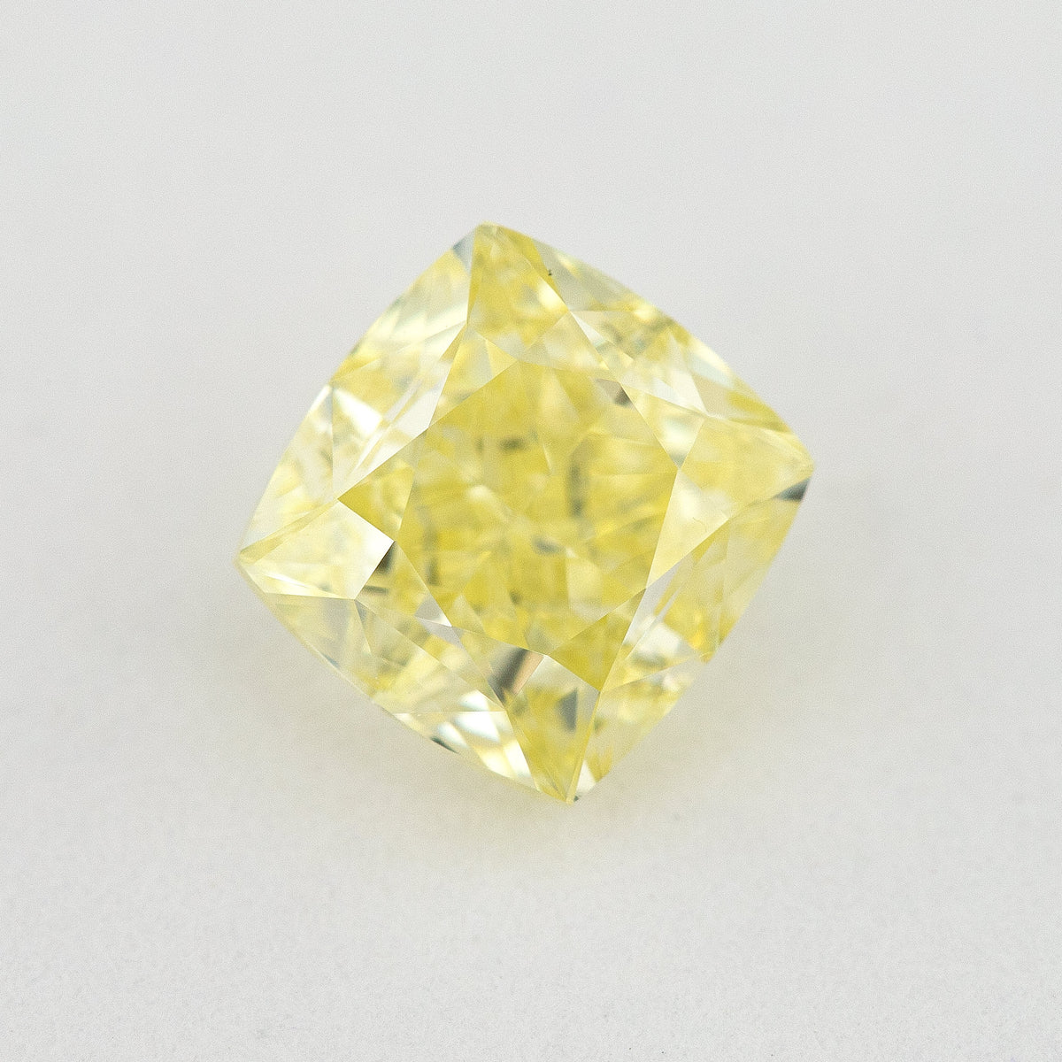 Face-up cushion-shaped yellow diamond on a pale surface, showing its complete outline, table and crown facets.