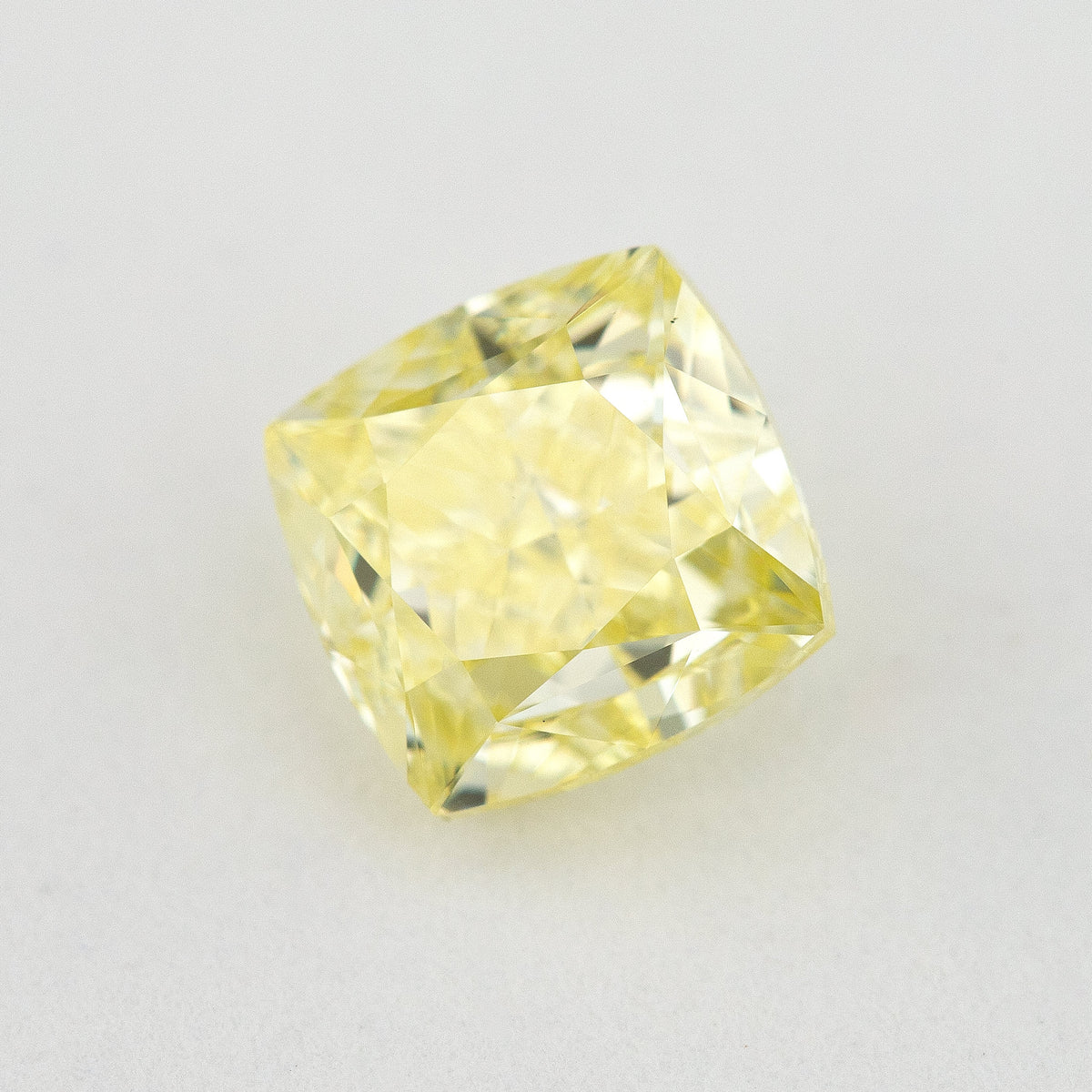 Angled crown view of the cushion-shaped yellow diamond on a pale surface, with bright reflected facets.