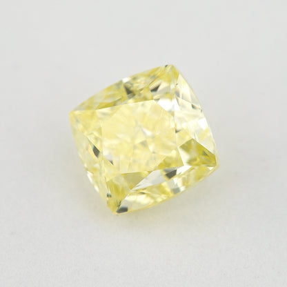 Angled crown view of the cushion-shaped yellow diamond on a pale surface, with bright reflected facets.