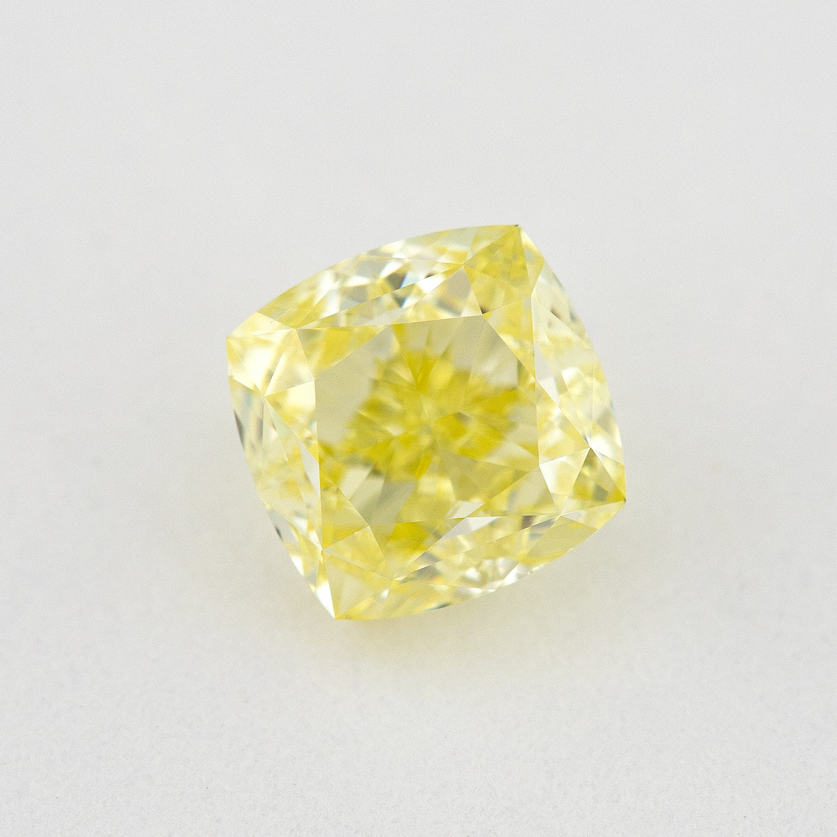 Face-up cushion-shaped yellow diamond on a pale surface, showing its outline, central table and bright crown facets.