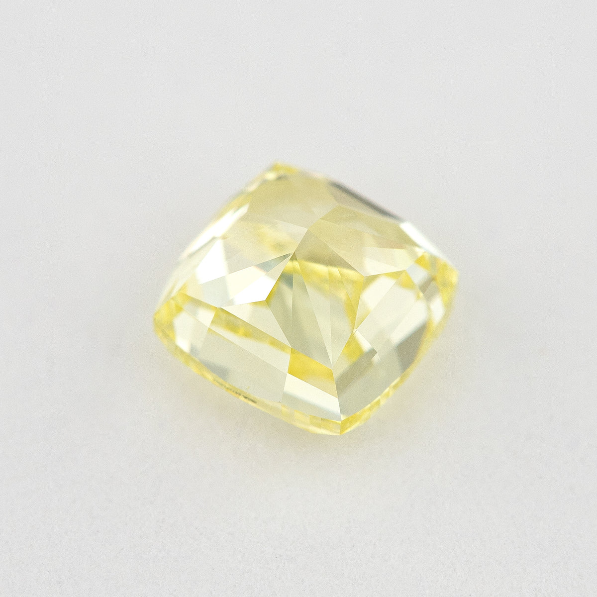 Pavilion and back view of the cushion-shaped yellow diamond on a pale surface, showing its broad rear facets.