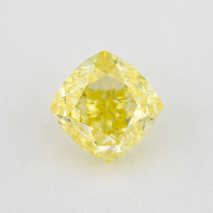 Face-up cushion-shaped yellow diamond on a pale surface, showing its complete outline, table and crown facets.