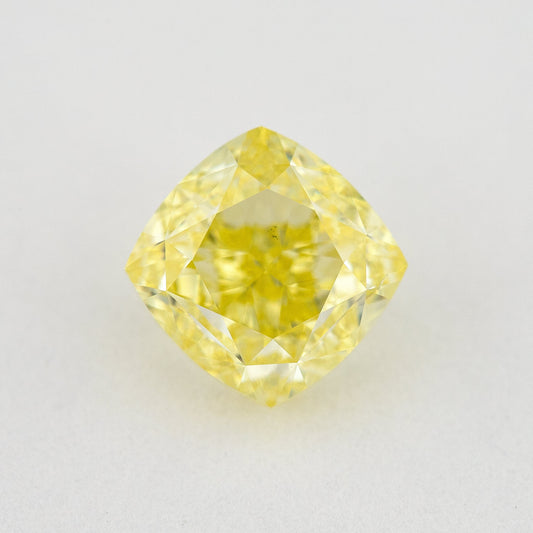Face-up cushion-shaped yellow diamond on a pale surface, showing its complete outline, table and crown facets.