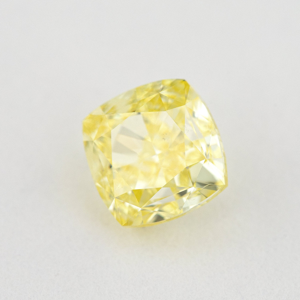 Angled crown view of the cushion-shaped yellow diamond on a pale surface, with bright reflected facets.