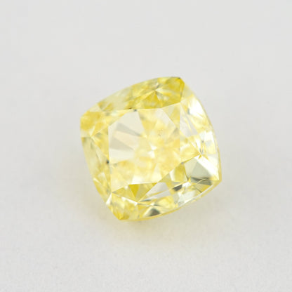 Angled crown view of the cushion-shaped yellow diamond on a pale surface, with bright reflected facets.