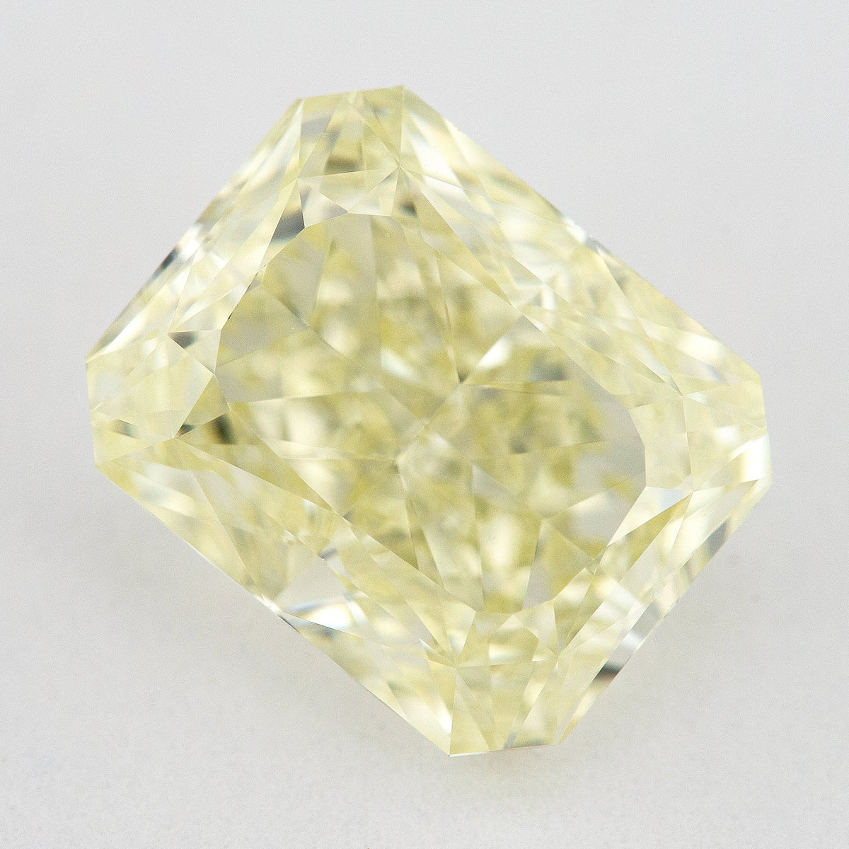 Face-up view of a pale yellow rectangular radiant-cut natural diamond on a pale surface, showing its complete outline and crown facets.