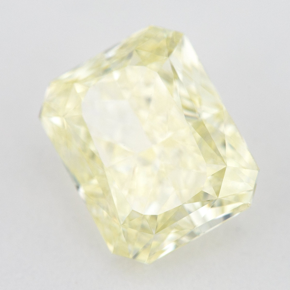 Tilted crown view of the pale yellow rectangular radiant-cut natural diamond, showing a different pattern of bright and dark facet reflections.