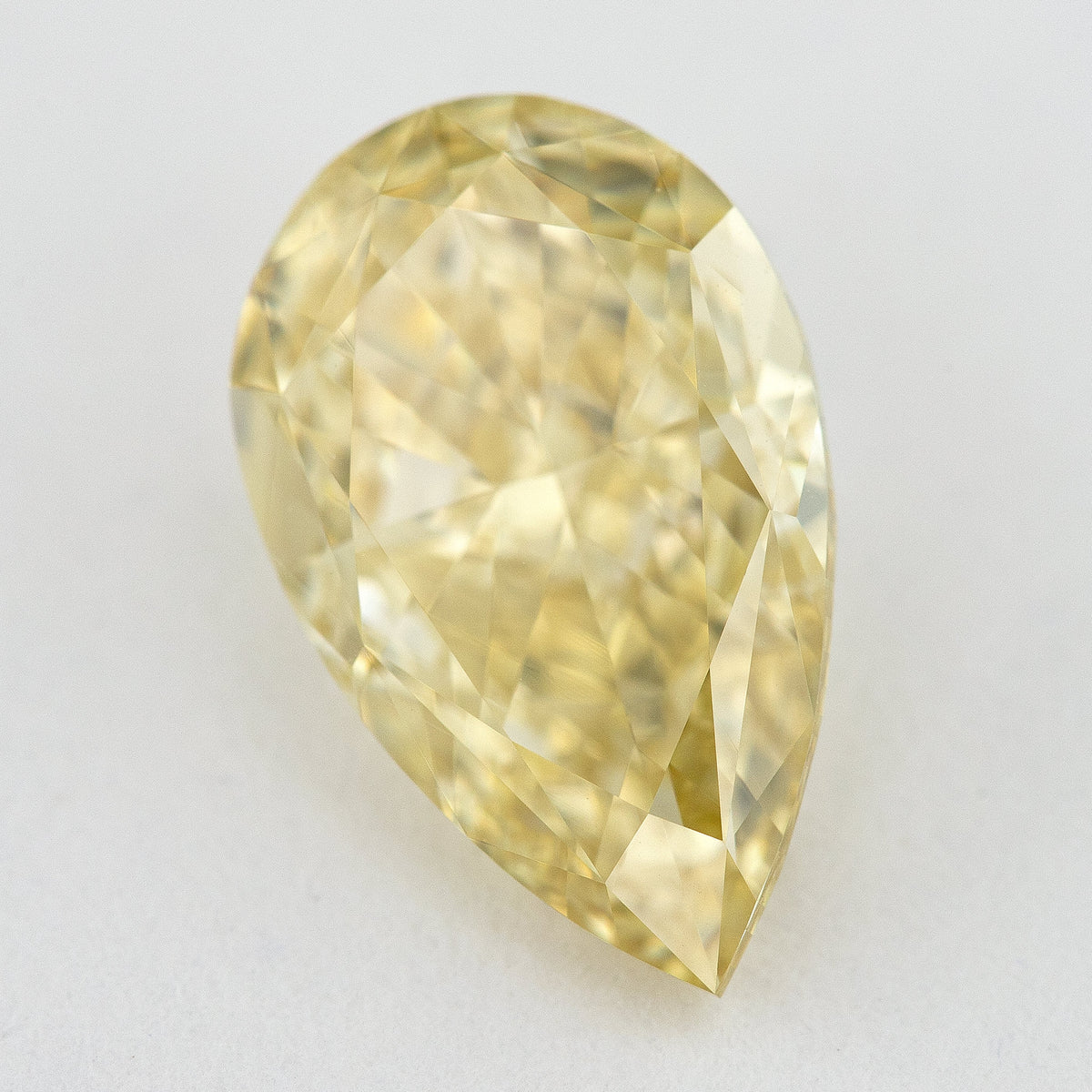 Alternate angled face-up view of the yellow pear diamond on a pale background, with a different pattern of light and dark facet reflections.