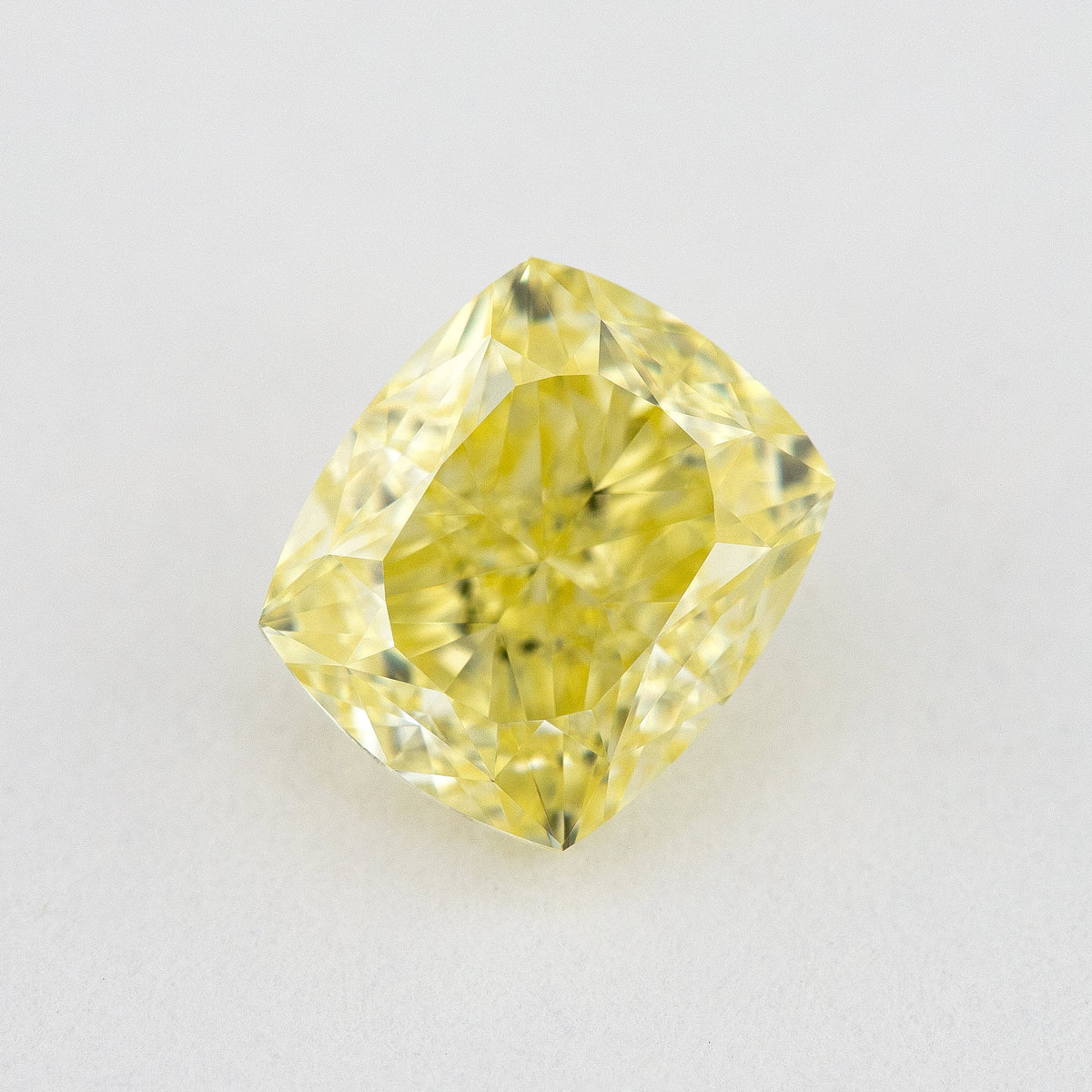 Face-up rectangular cushion-shaped yellow diamond on a pale background, showing yellow table reflections and bright facets.