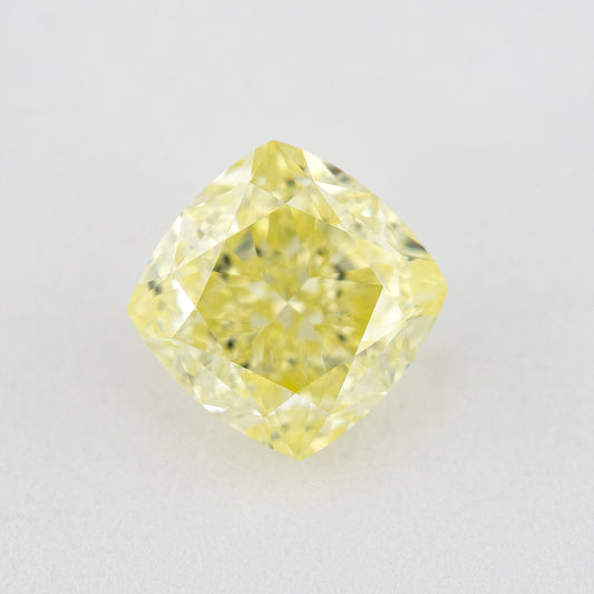 Face-up cushion-shaped yellow diamond on a pale surface, showing its complete outline, table and crown facets.