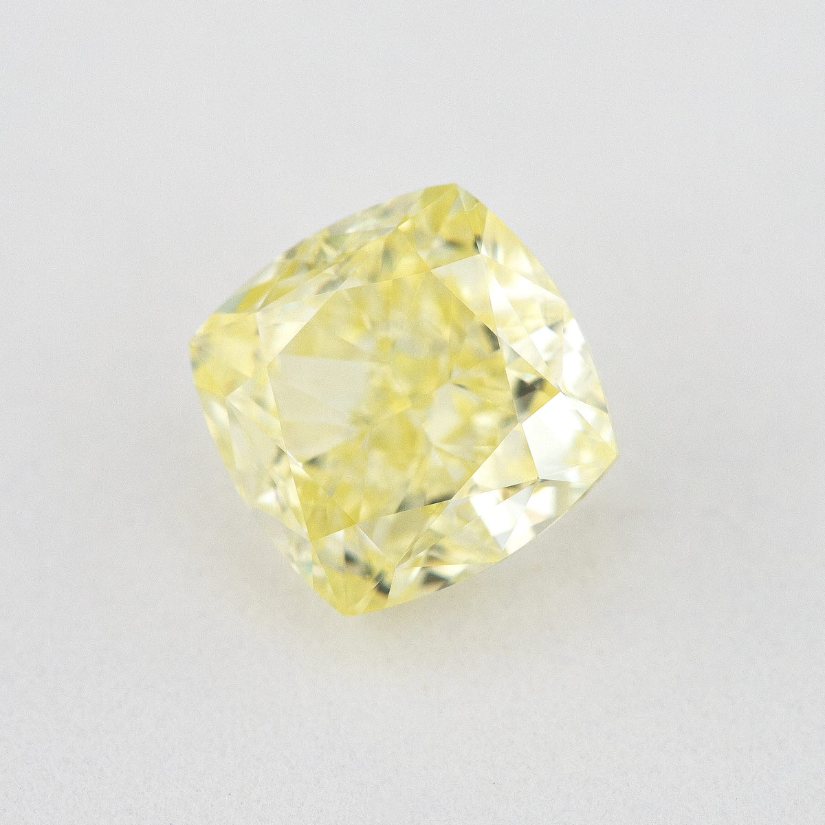 Angled crown view of the cushion-shaped yellow diamond on a pale surface, with bright reflected facets.