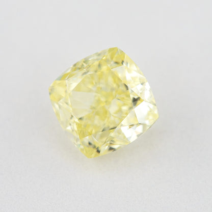 Angled crown view of the cushion-shaped yellow diamond on a pale surface, with bright reflected facets.
