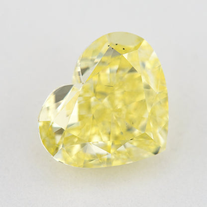 Face-up view of a yellow heart-shaped natural diamond on a pale surface, showing its complete outline and crown facets.