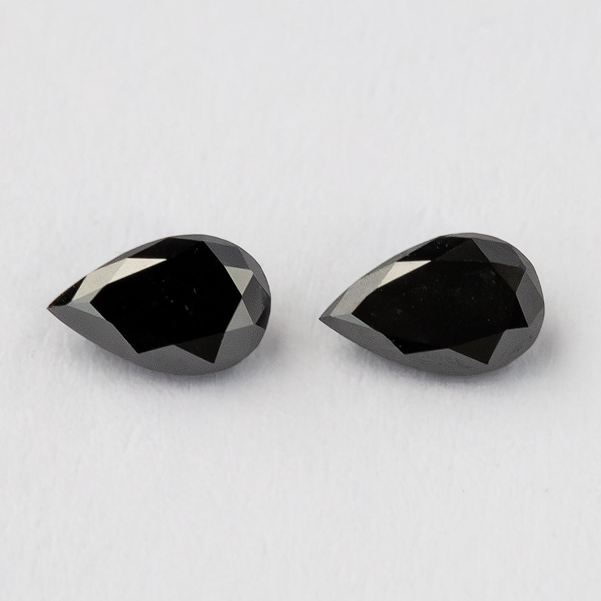 Two black pear-shaped diamonds face-up on a white surface, with dark tables and bright crown-edge reflections.