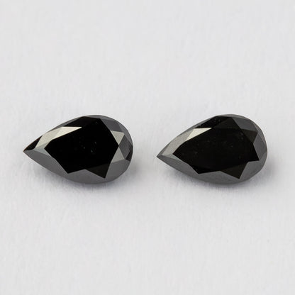 Two black pear-shaped diamonds face-up on a white surface, with dark tables and bright crown-edge reflections.