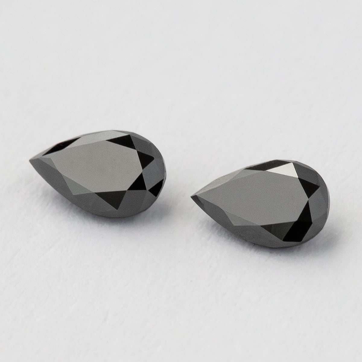 Angled view of the black pear-shaped diamond pair, with broad pale reflections across their tables.